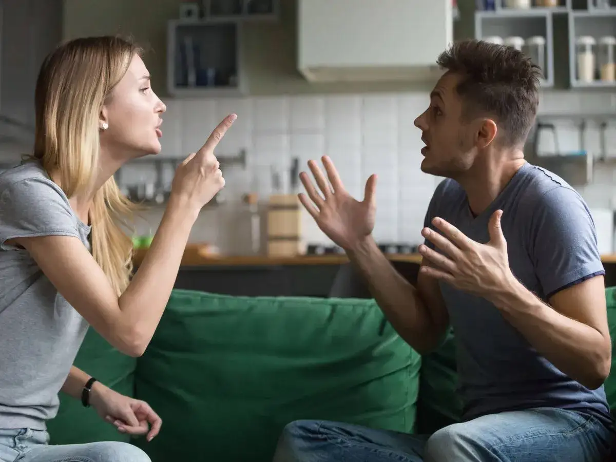 Pareja discutiendo acaloradamente en el sof&aacute;, con gestos enf&aacute;ticos. Claros problemas conyugales en el aire.