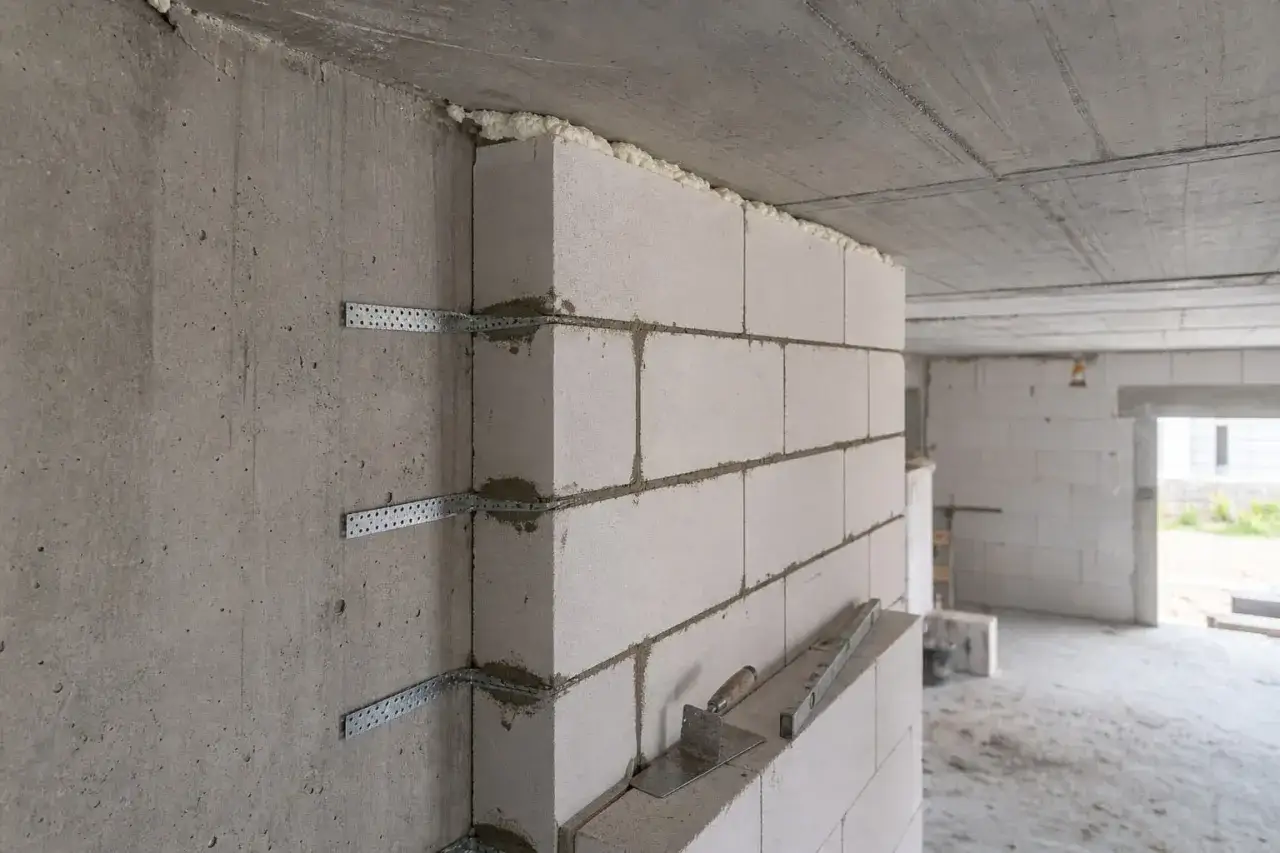 Betonowe ściany nośne łączone z bloczków zbrojone metalowymi kątownikami. Widać narzędzia budowlane.