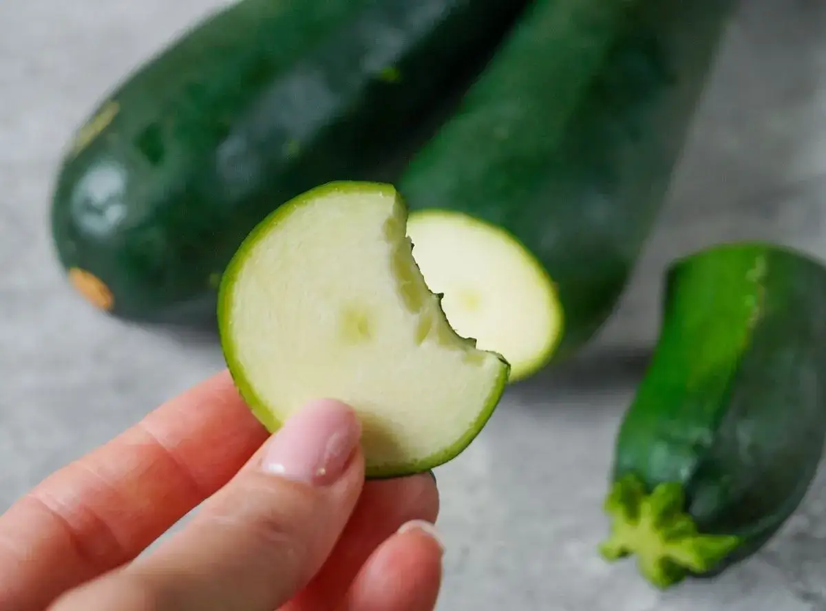 Ein Stück Zucchini roh essen – erfrischend und gesund! Mehrere grüne Zucchinis liegen auf grauem Untergrund.