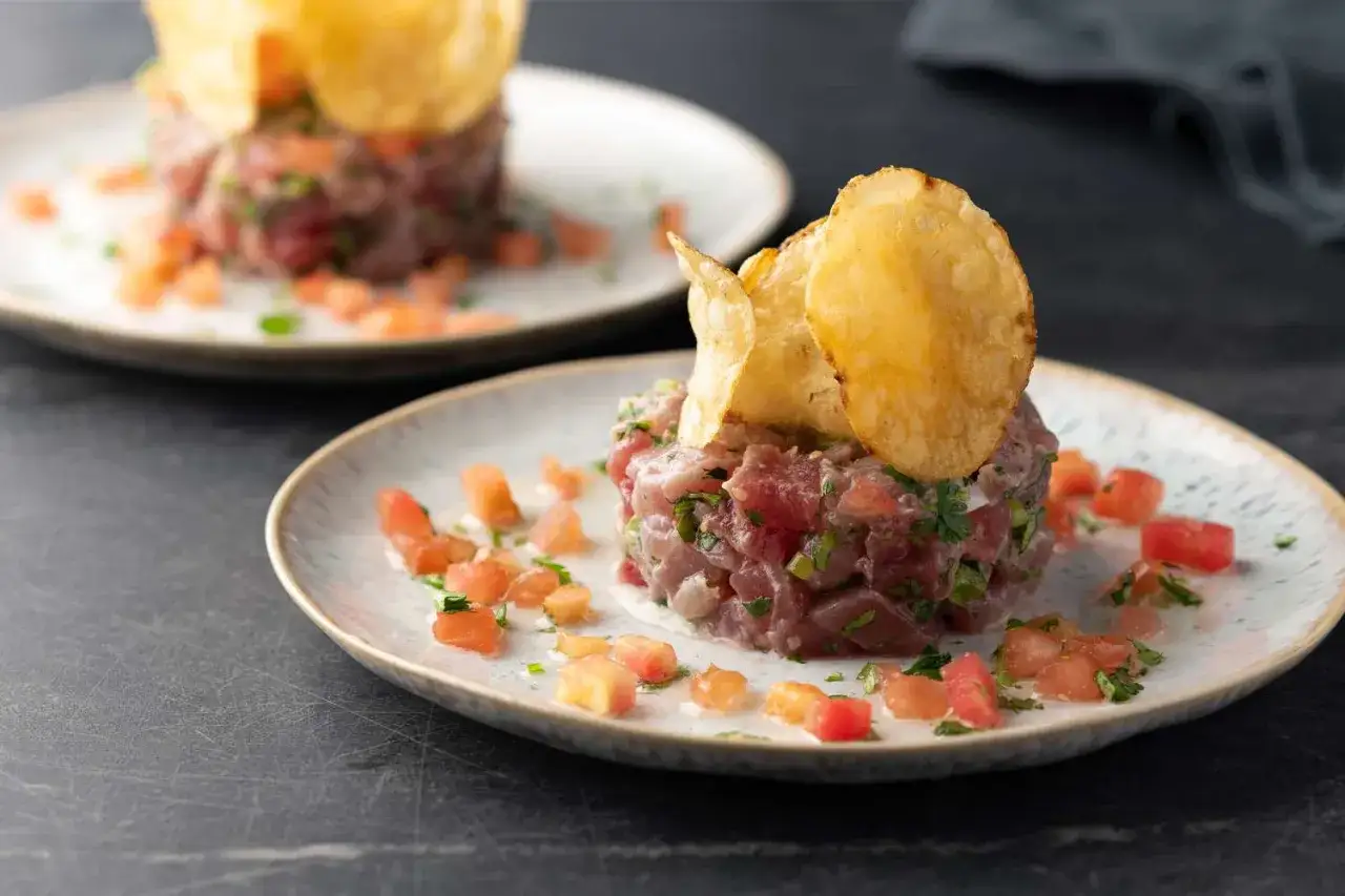 Deux assiettes de tartare de thon frais, garnies de dés de tomates et de chips croustillantes. Un délice visuel et gustatif.