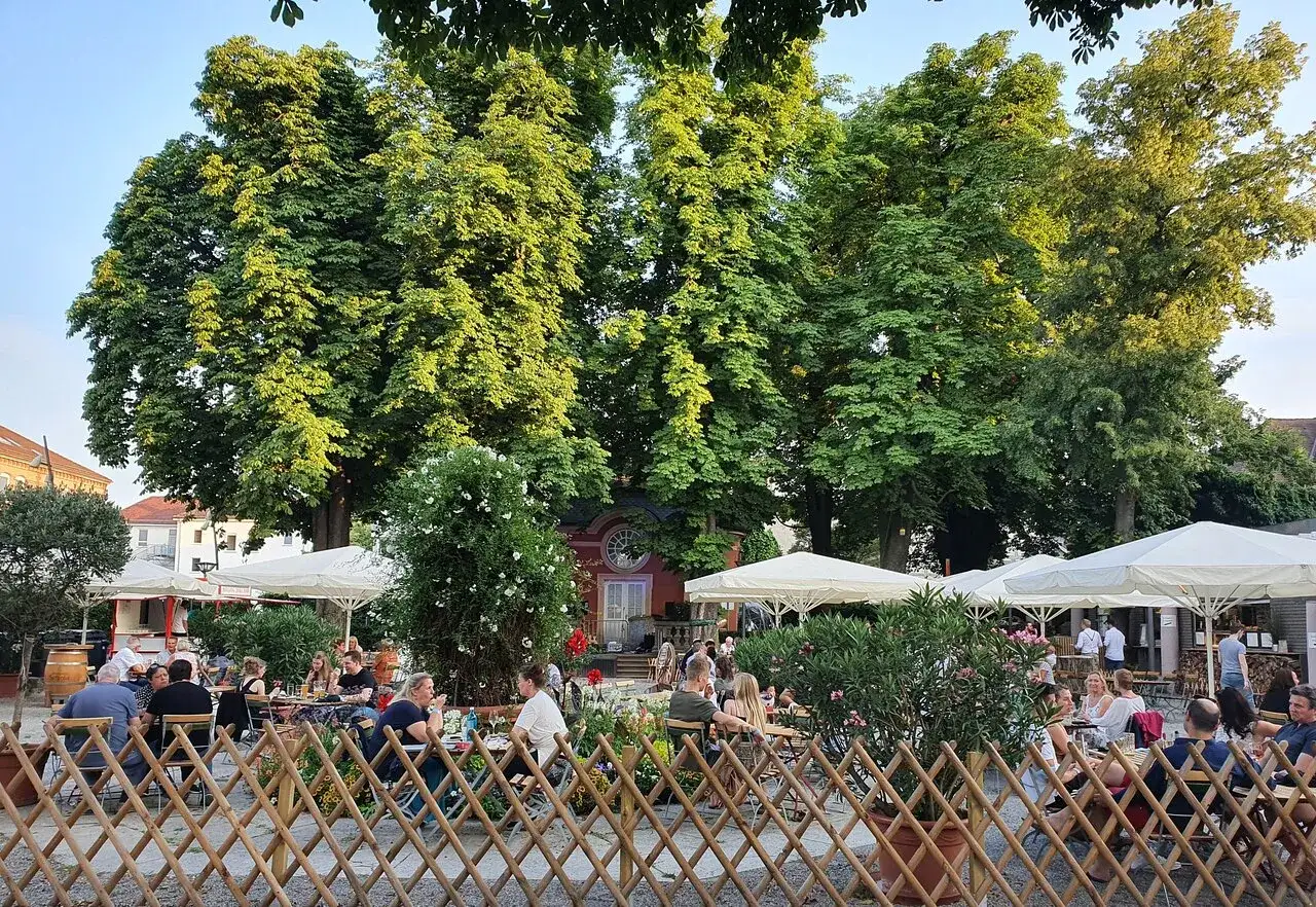 Gem&uuml;tlicher Biergarten am Ratskeller Ludwigsburg unter schattigen B&auml;umen. G&auml;ste genie&szlig;en das Beisammensein.