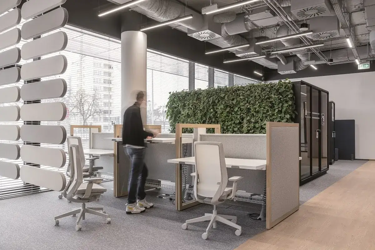 Un homme se d&eacute;place dans un espace de travail open space moderne avec des bureaux, des cloisons acoustiques et un mur v&eacute;g&eacute;tal luxuriant.