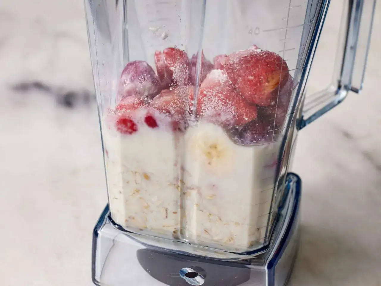 Ein Mixer mit gefrorenen Erdbeeren, Banane, Milch und Haferflocken für einen gesunden smoothie mit haferflocken.