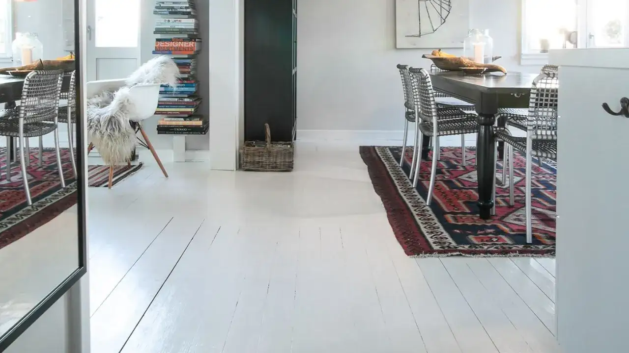 Vitt målat furugolv i en ljus matsal med en stor matta och stolar runt ett mörkt träbord.