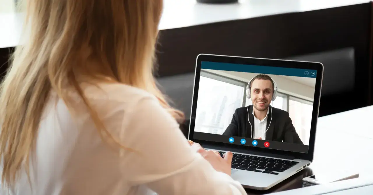 Kobieta prowadzi rozmowy rekrutacyjne online. Na ekranie laptopa widać uśmiechniętego mężczyznę w słuchawkach.