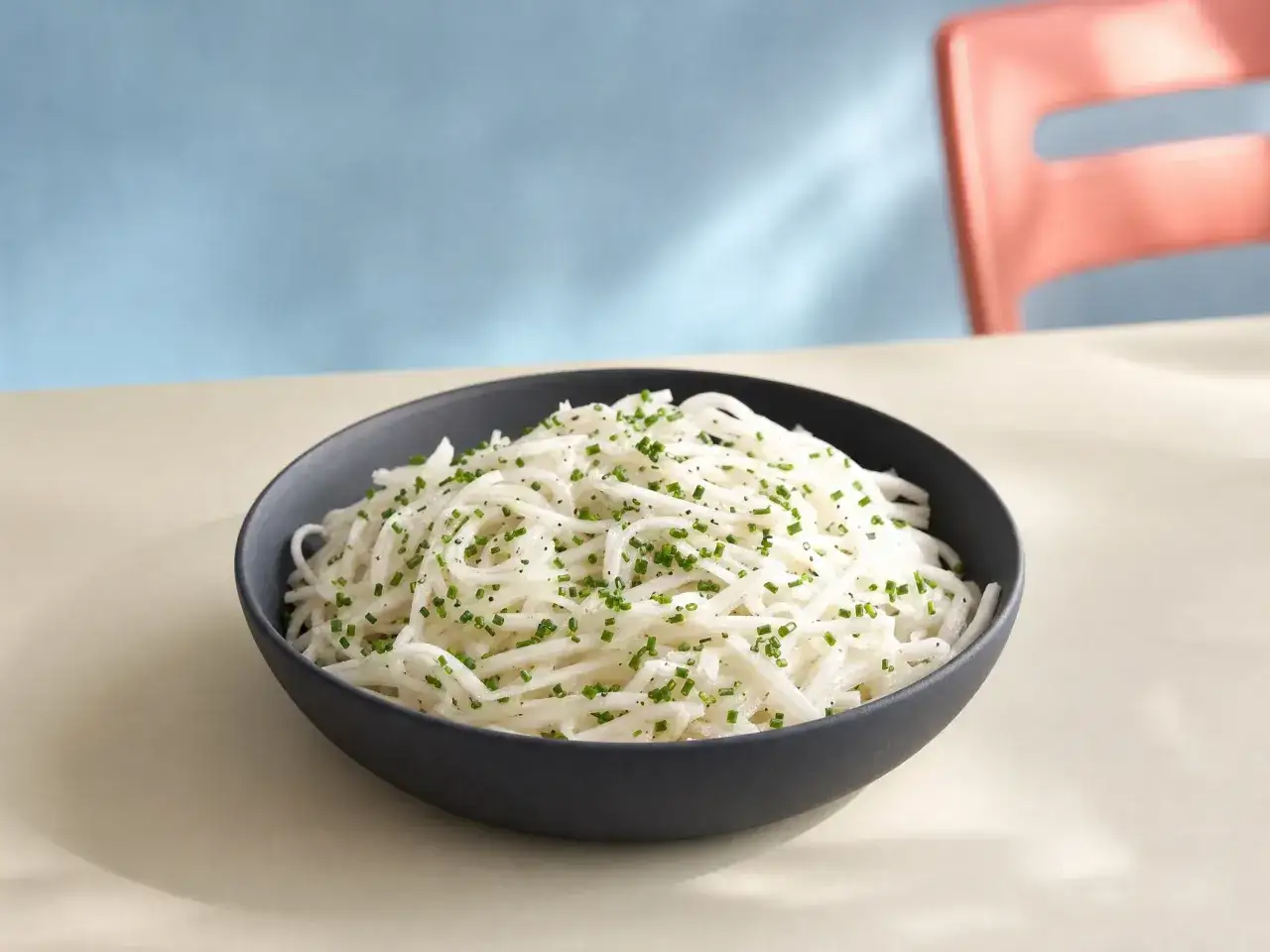 Ein Schüssel mit feinen Rettichstreifen, garniert mit Schnittlauch und Pfeffer. Perfekt für ein leichtes Rettichsalat Rezept.
