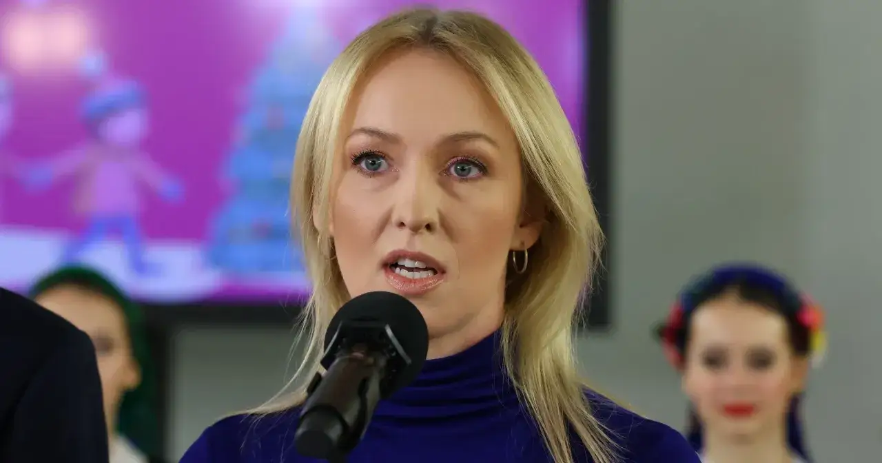 Urszula Brzezińska Hołownia, mówiąca do mikrofonu, w tle dzieci w strojach ludowych.