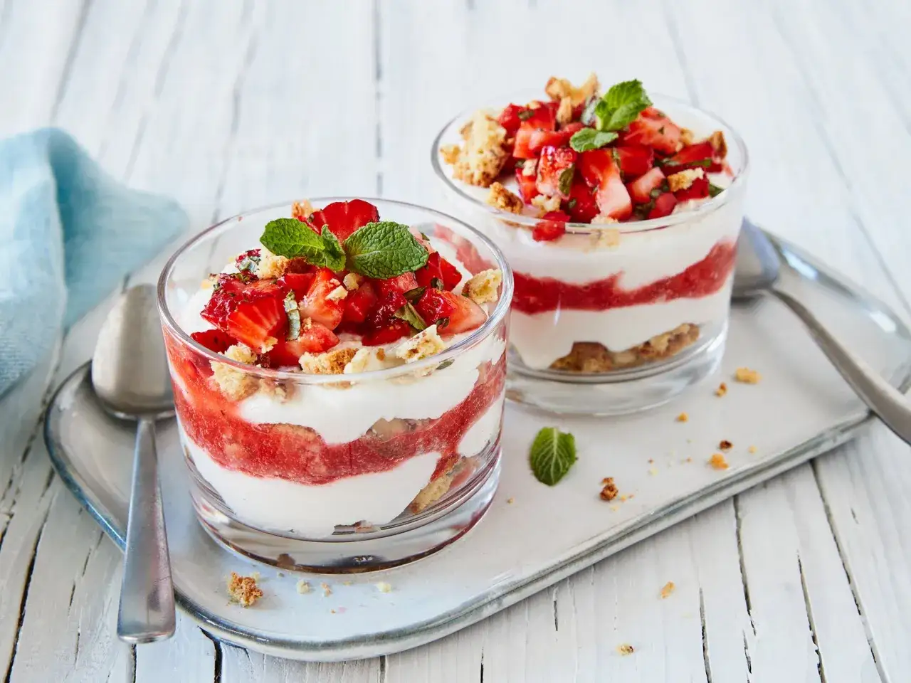 Zwei Gl&auml;ser mit einem k&ouml;stlichen Dessert mit Erdbeeren, Sahne und Kekskr&uuml;meln, garniert mit Minze.