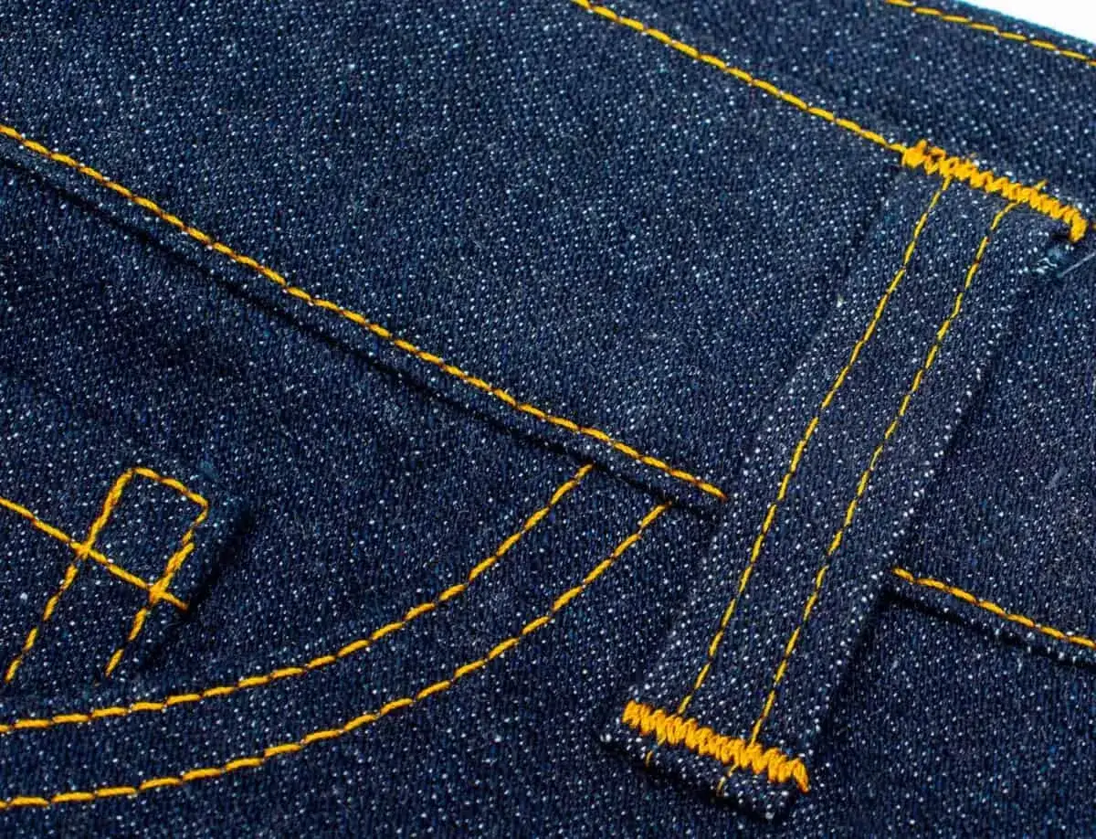 Close-up of dark blue denim with bright yellow stitching, highlighting the sturdy belt loop pattern and pocket details.