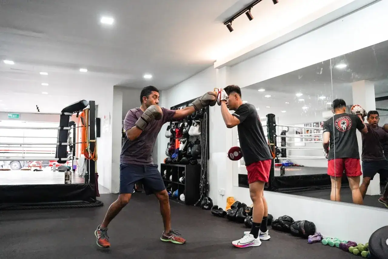 Two men are sparring in a boxing gym. One throws a punch while the other blocks, demonstrating that sparring is a sport.