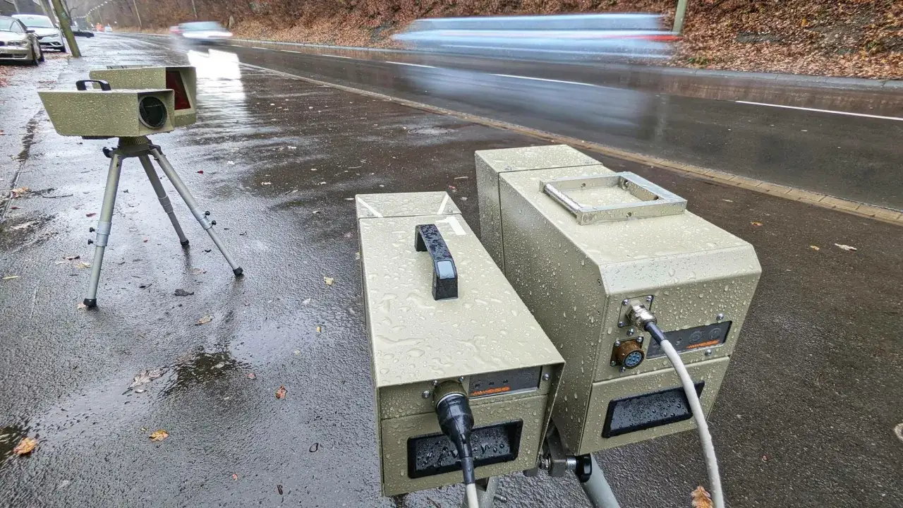 Zwei Messger&auml;te, ein motorrad blitzer und ein weiteres Ger&auml;t, stehen auf einem nassen Asphalt. Im Hintergrund verschwimmen vorbeifahrende Autos.