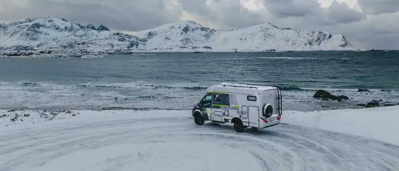Husbil vid sn&ouml;ig strand i Norge, perfekt f&ouml;r ett sportlov. Vackra sn&ouml;kl&auml;dda berg i bakgrunden.
