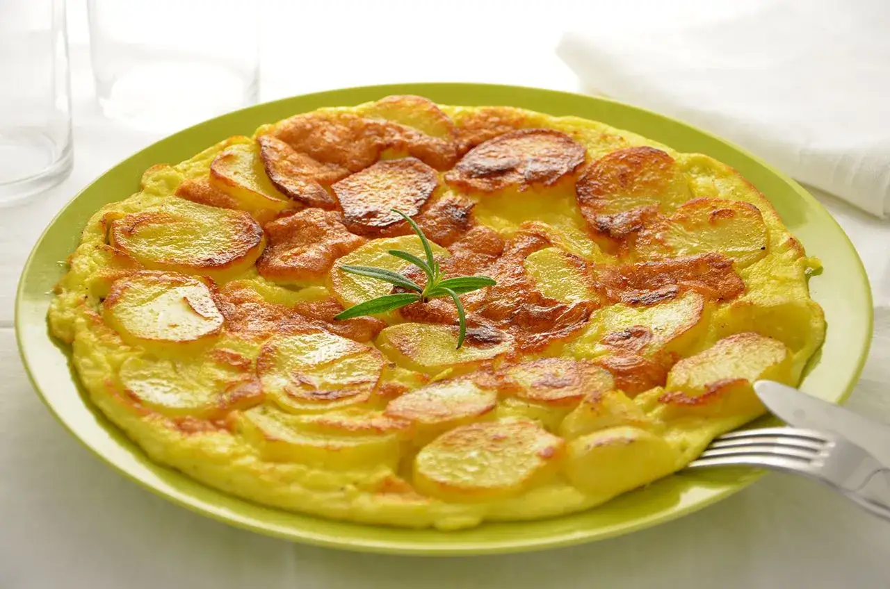 Una deliziosa ricetta frittata di patate, dorata e gustosa, guarnita con rosmarino fresco su un piatto verde.