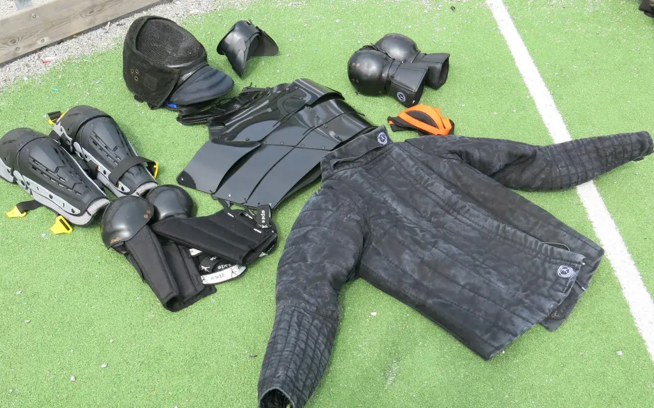 Utrustning f&ouml;r hema kampsport: vadderad jacka, hj&auml;lm, benskydd, armskydd och en br&ouml;stpl&aring;t.