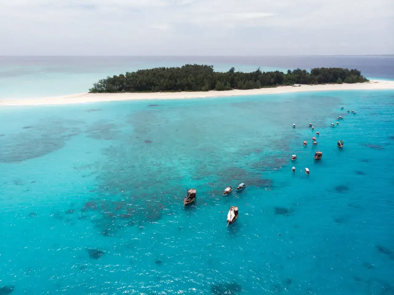 Zanzibar w czerwcu: turkusowa woda, piaszczysta wyspa i łodzie z turystami. Idealna pogoda na snorkeling.