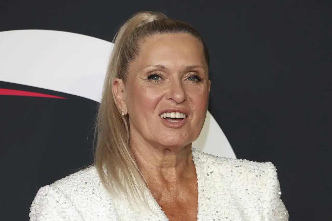 Uśmiechnięta Ewa Kasprzyk w białej, cekinowej marynarce, z blond kucykiem.