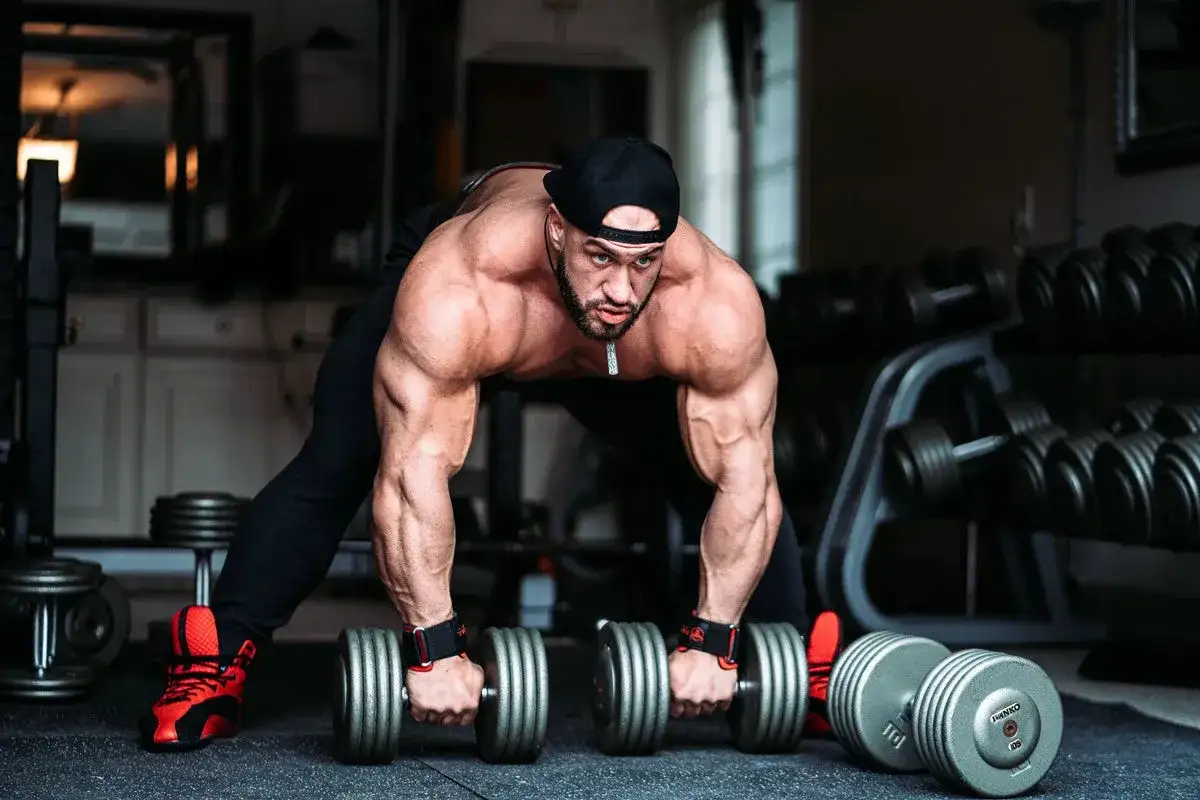 Muskulös man tränar ben med hantlar i ett gym.