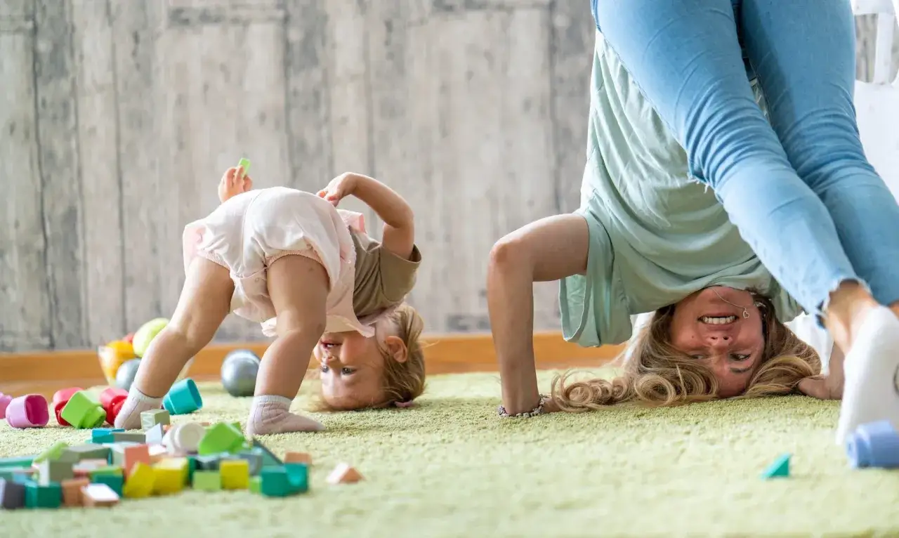 Bambina e adulta in posa yoga, circondate da giocattoli. Un esempio di come le competenze non cognitive si sviluppano giocando.