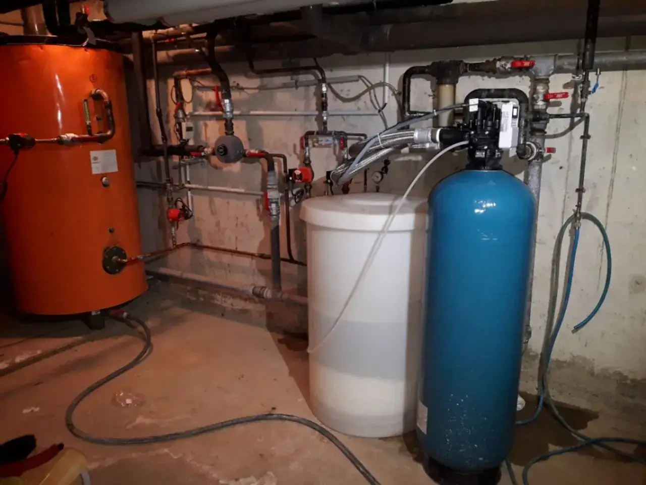 Système de plomberie avec un chauffe-eau orange et un adoucisseur nouvelle génération bleu, prêt à améliorer la qualité de l'eau.