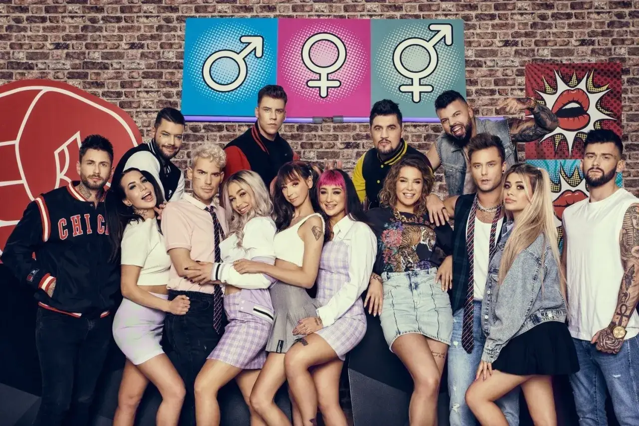 Warsaw Shore obsada pozuje do zdjęcia. Grupa młodych ludzi w modnych stylizacjach, na tle ceglanej ściany i kolorowych symboli płci.