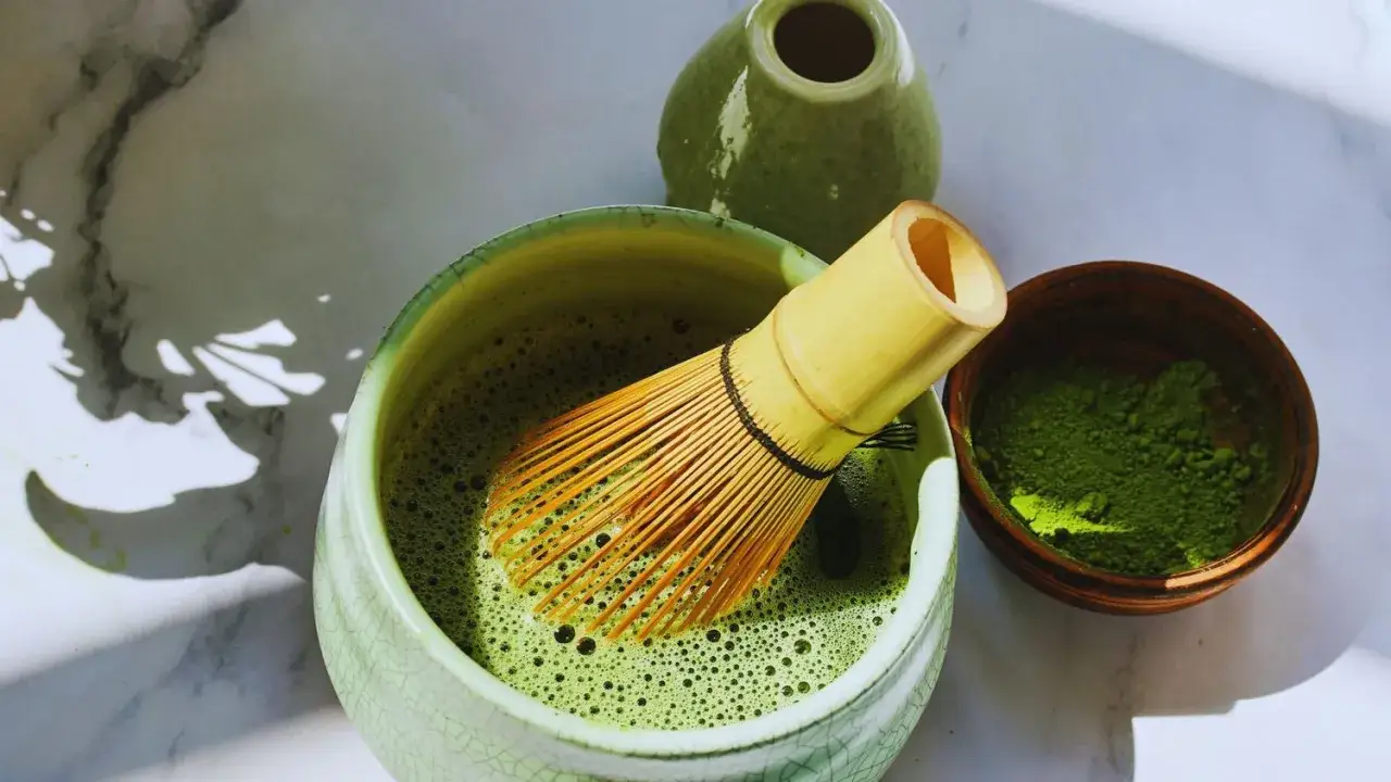 Un bol de matcha mousseux avec un fouet en bambou, une petite coupelle de poudre verte et un pot. C'est &ccedil;a le matcha !
