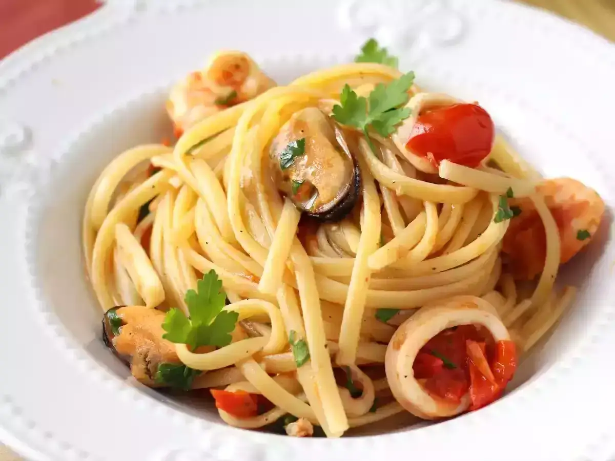 Tallarines con gambas al ajillo, mejillones, calamares y tomates cherry, decorados con perejil fresco.