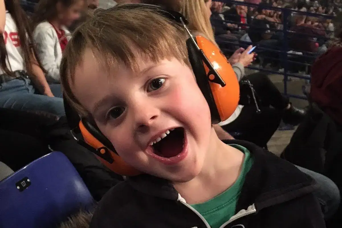 Un jeune garçon de 3 ans, avec un bouchon oreille enfant 3 ans, s'exclame joyeusement dans une foule.