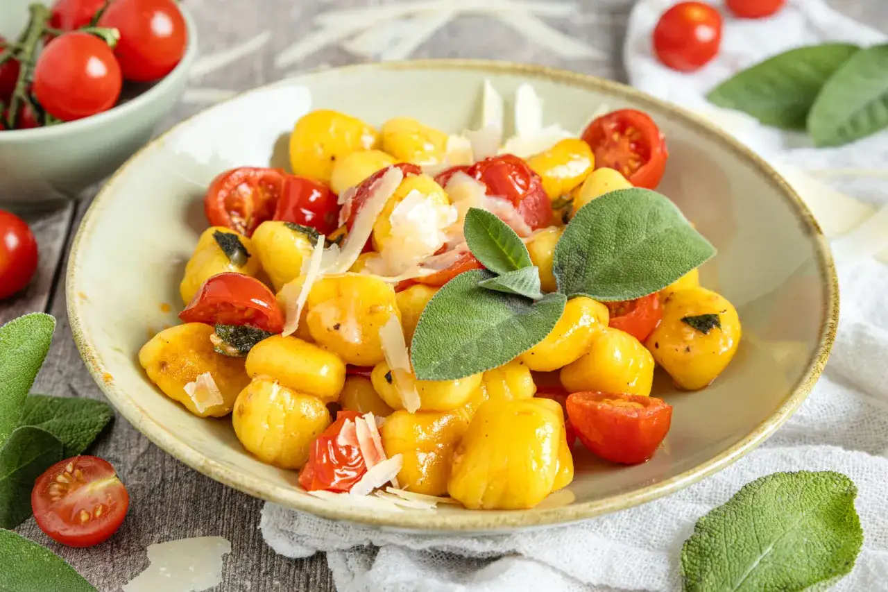 Goldgelbe salbei gnocchi mit Kirschtomaten und Parmesan, garniert mit frischen Salbeiblättern. Ein Genuss für Gaumen und Auge.