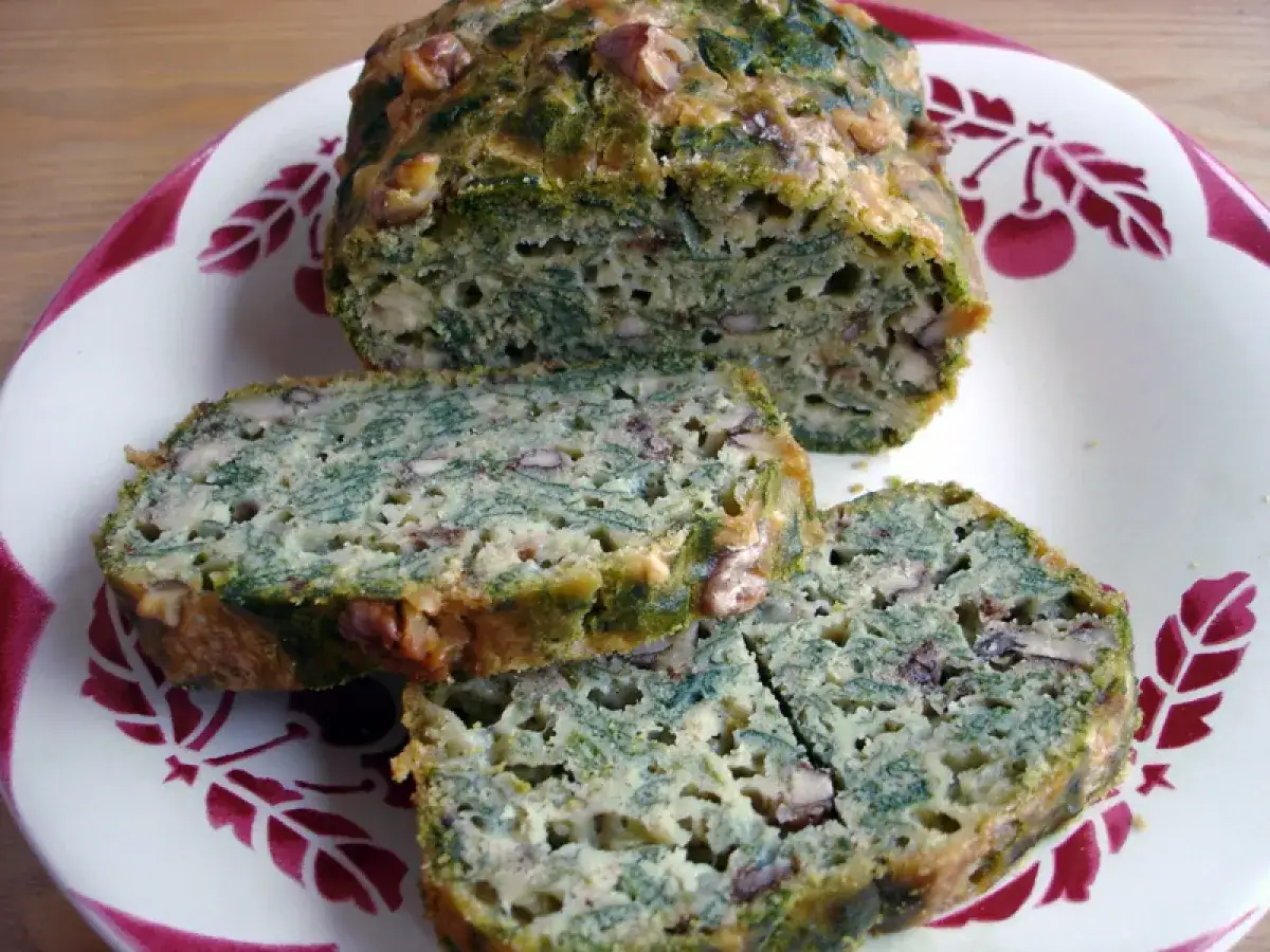 Tranches d'un cake aux orties et noix, sur une assiette décorée de cerises.