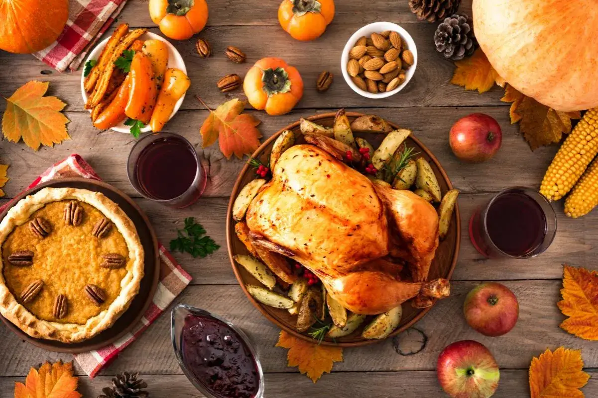 Una mesa festiva para el dia de accion de gracias en ingles, con pavo asado, pastel de calabaza, maíz, frutas y vino.
