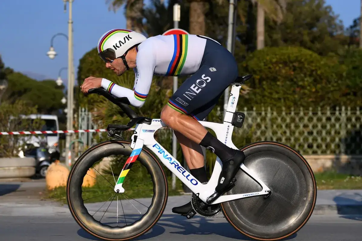 Cyclist in rainbow stripes helmet and INEOS kit races a time trial bike, pushing hard for a Tour de France victory.