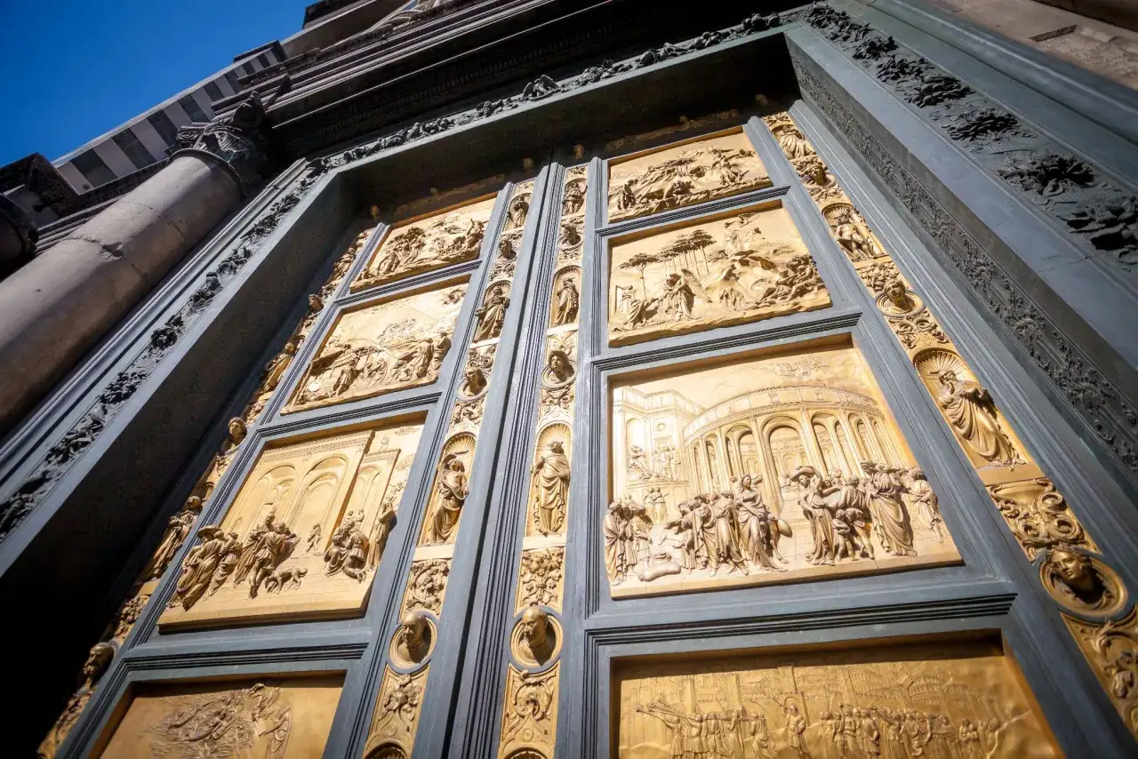 Las puertas del paraíso, con sus relieves dorados narrando historias bíblicas, se alzan majestuosas bajo un cielo azul intenso.