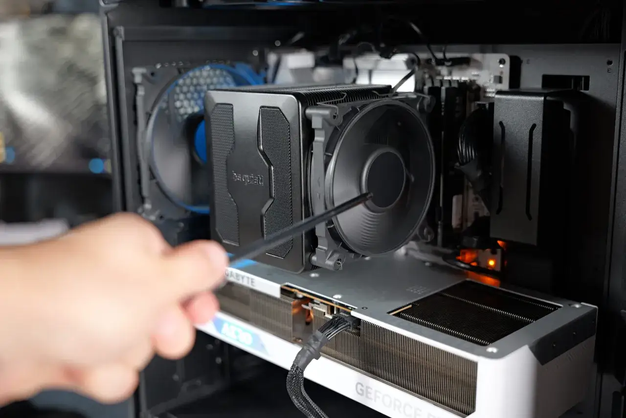 Wnętrze komputera z widocznymi częściami: cooler CPU, karta graficzna Gigabyte AERO, wentylatory i okablowanie. Dłoń z narzędziem przy coolerze.