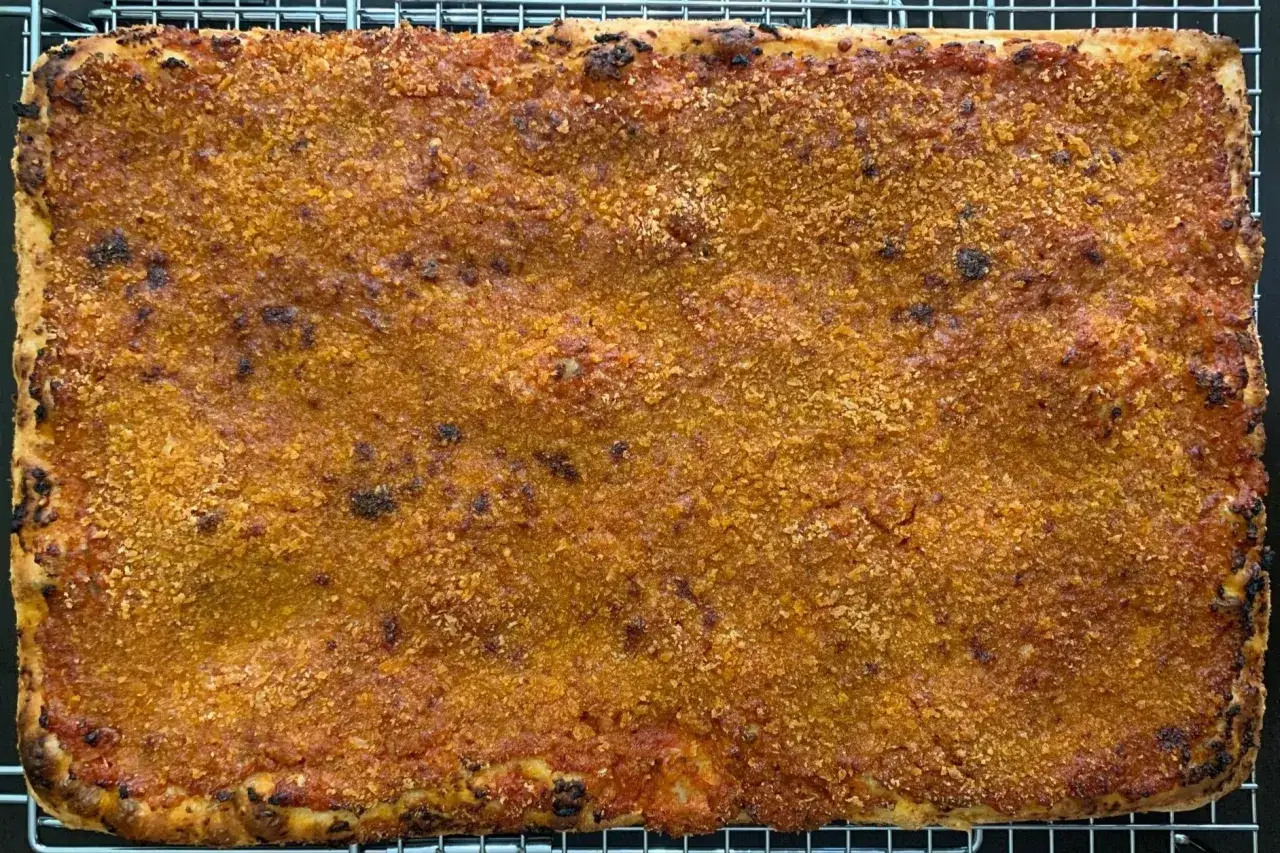 Prostokątna pizza sycylijska z chrupiącą, złocistą posypką na wierzchu, lekko przypieczona na brzegach.