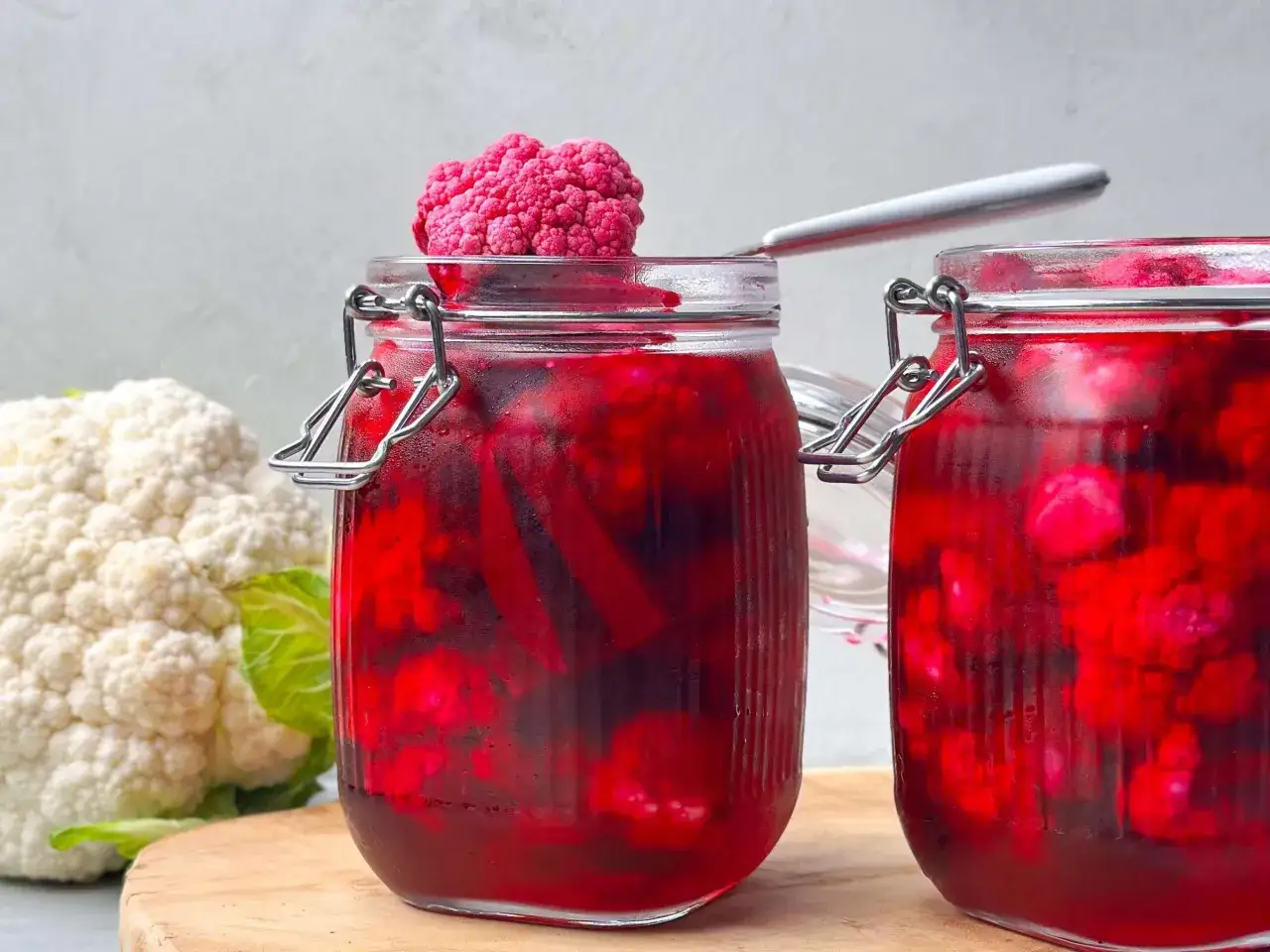 Zwei Gläser mit eingelegtem Blumenkohl in roter Lake. Ein kleiner rosa Blumenkohl thront auf dem Deckel.