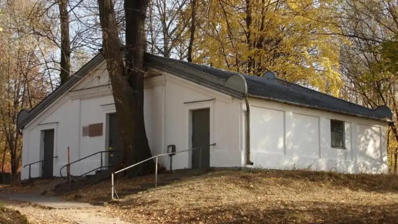 Ohel cadyka Elimelecha w Leżajsku zwiedzanie. Biały budynek z drzwiami i oknem, otoczony drzewami jesienią.