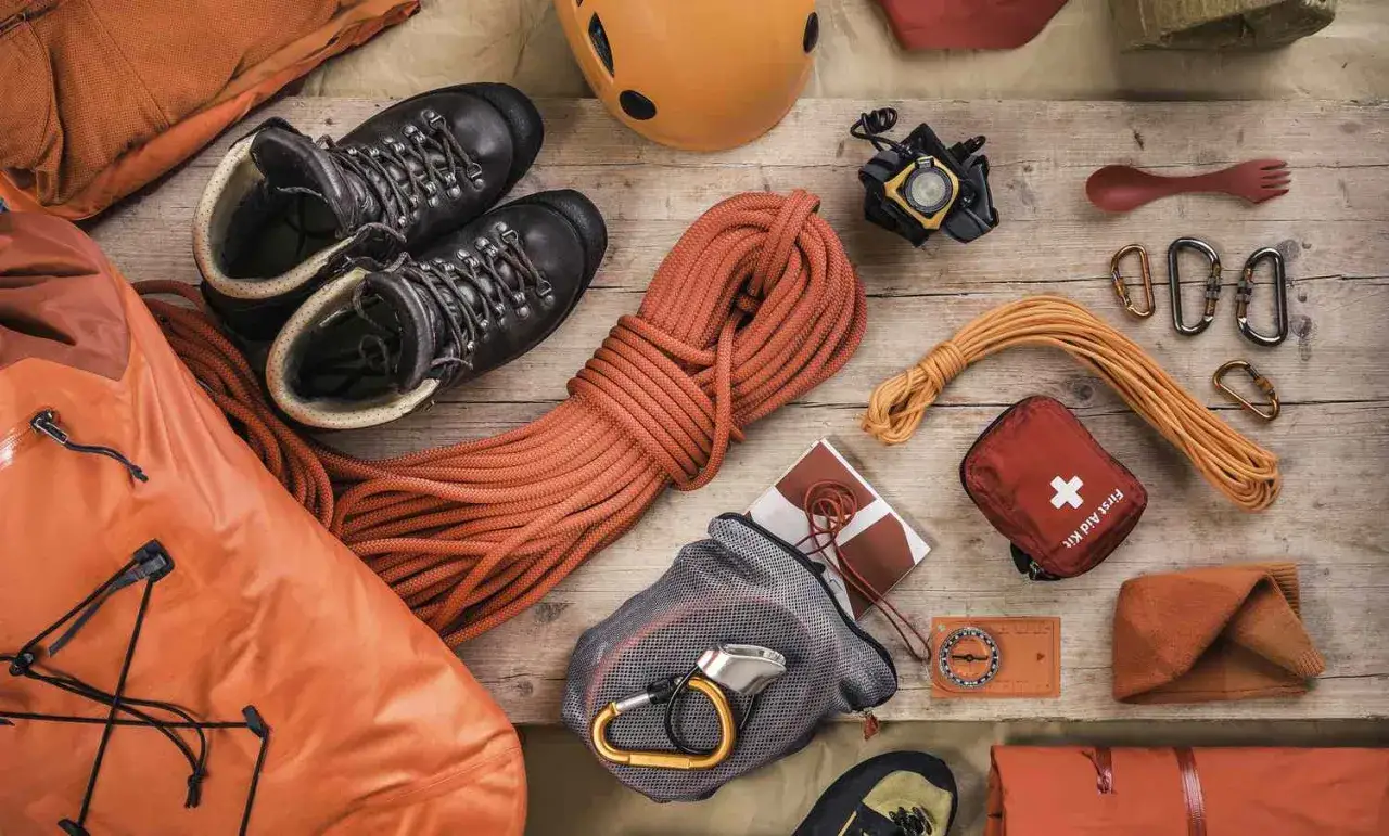 Vue aérienne d'une liste de matériel d'escalade : chaussures, cordes, casque, mousquetons, trousse de premiers secours, boussole et sac étanche.