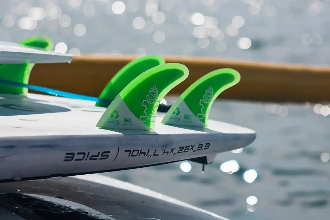 Gr&uuml;ne Finnen auf einem wei&szlig;en SUP-Board. Die Finnen haben ein Logo und Recycling-Symbole. Man sieht, dass die SUP Finnen Unterschiede in der Form haben.