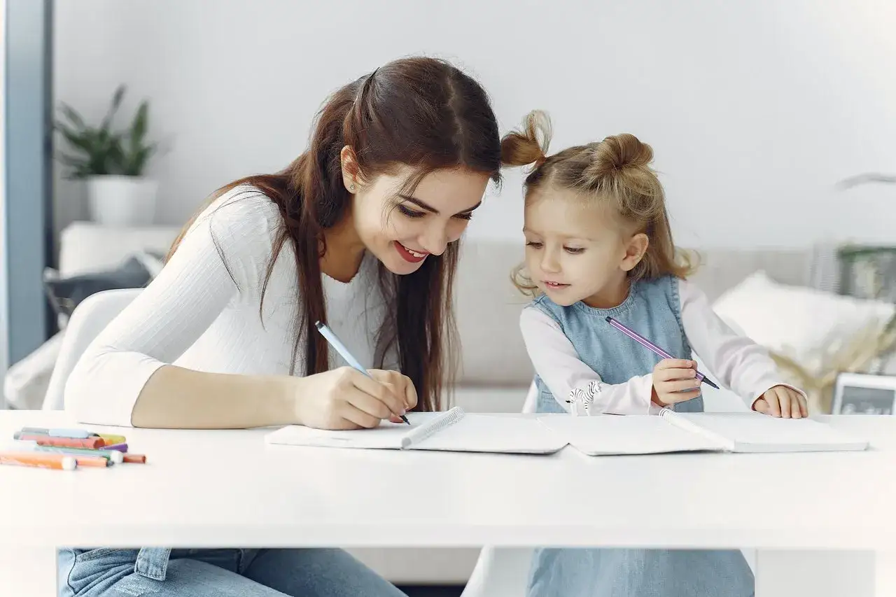 Mama na urlopie rodzicielskim uczy córkę pisać. Rysują razem w zeszytach, czerpiąc radość ze wspólnego czasu.