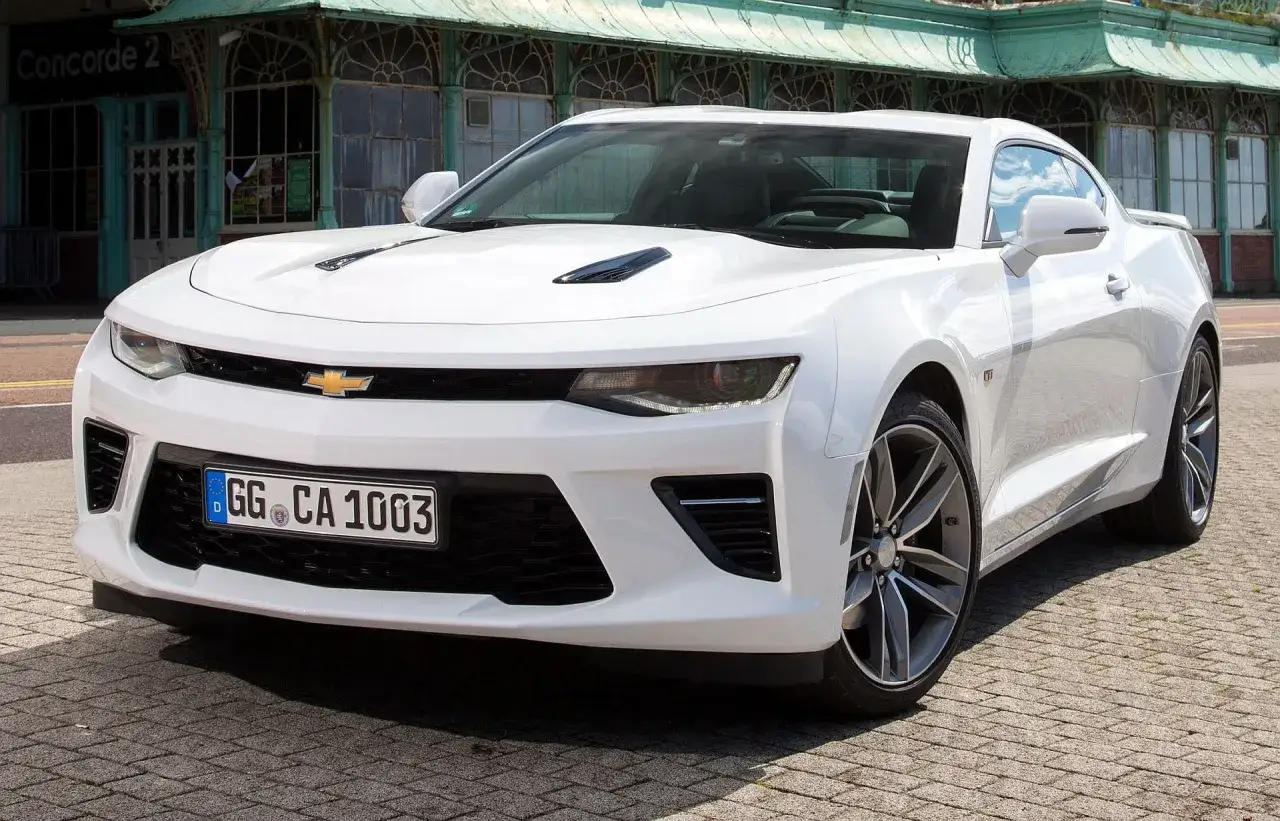 Biały Chevrolet Camaro, marzenie o tanich sportowych autach, zaparkowany na bruku przed zabytkowym budynkiem.
