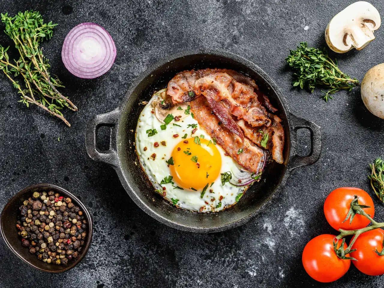 &OElig;uf au plat air fryer avec bacon croustillant, servi dans une po&ecirc;le en fonte, entour&eacute; de tomates, d'oignons rouges, de champignons et de poivre.