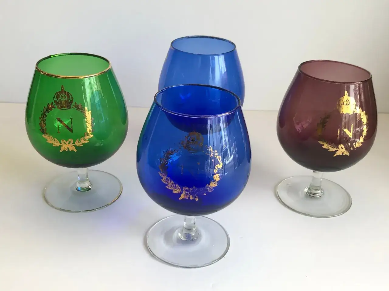Cztery kieliszki do brandy w kolorach zielonym, niebieskim i fioletowym, ozdobione złotym monogramem 