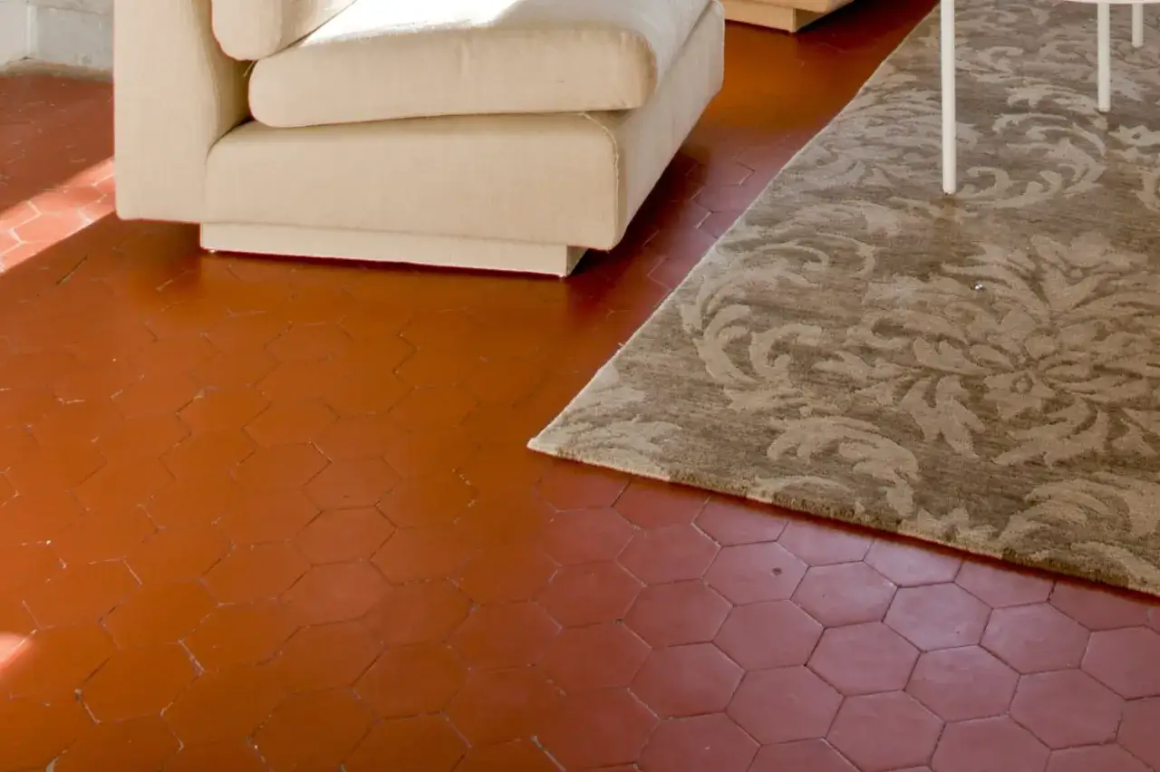 Un salon avec un canap&eacute; beige et un tapis orn&eacute;, sur un sol en carrelage hexagonal rouge. Id&eacute;al pour nettoyer carrelage poreux.