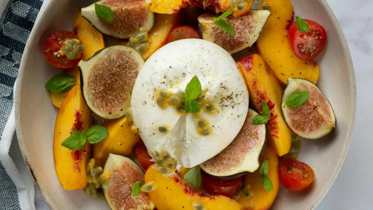 Ein cremiger Burrata-Käse umgeben von saftigen Pfirsichen, Feigen, Kirschtomaten und Passionsfrucht. Was ist Burrata? Ein Genuss!