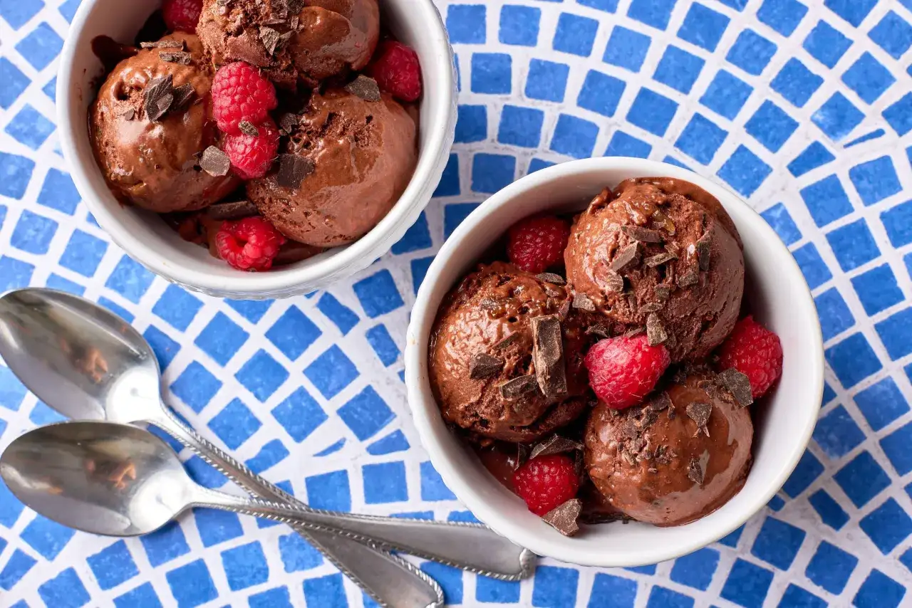 Zwei Schalen mit cremigem Schokoladen-nice-cream, garniert mit Himbeeren und Schokostückchen, daneben zwei Löffel.
