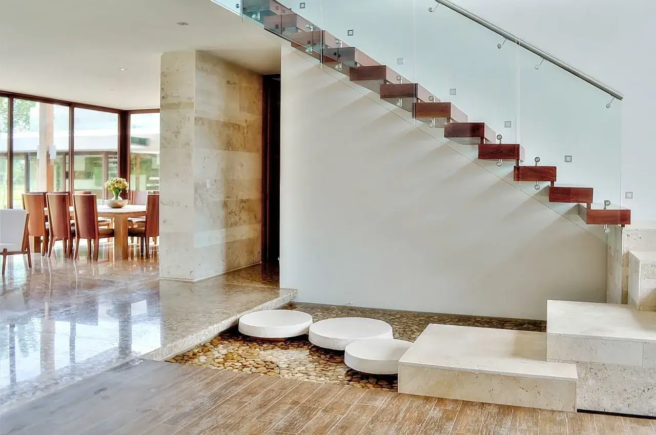 Escalera de madera flotante con barandilla de cristal. Ideas para decorar una escalera de madera con un estanque de guijarros y piedras.