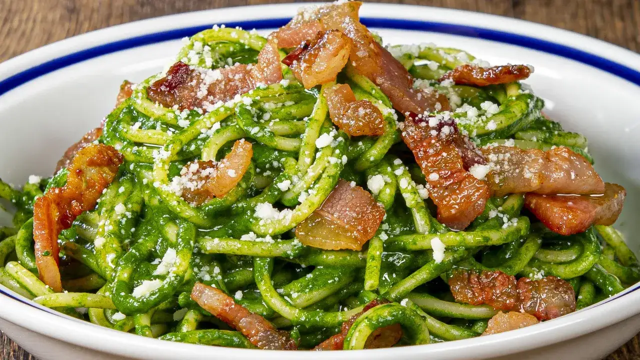 Pasta con spinaci e pancetta croccante, un piatto colorato e saporito, cosparso di formaggio grattugiato.