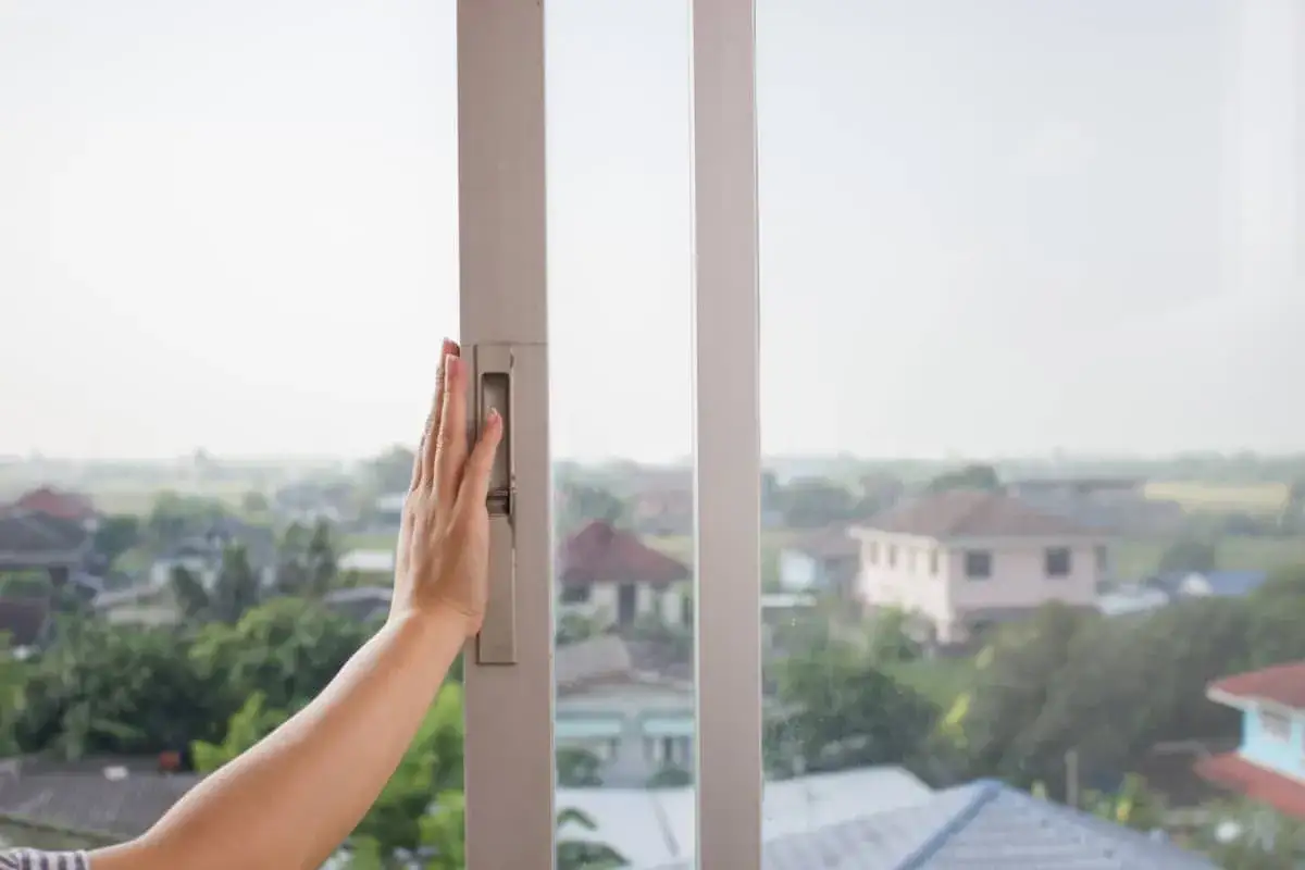 Mano sujetando el marco de una ventana corredera, &uacute;til para saber como aislar ventanas correderas y mejorar la eficiencia energ&eacute;tica.