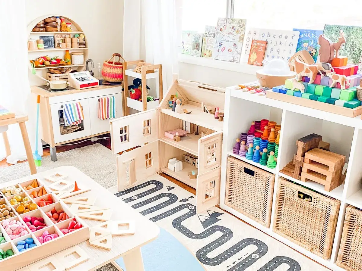 Un cuarto de juegos lleno de juguetes de madera, una casa de muñecas, bloques de construcción y una cocina de juguete. Todo listo para guardar y jugar.