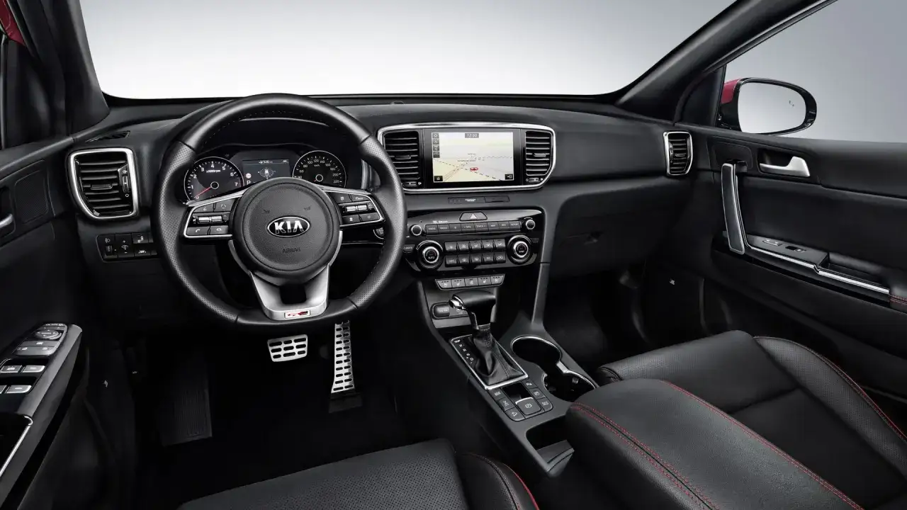 Wnętrze Kia Sportage 2018: czarna skórzana tapicerka z czerwonymi przeszyciami, multimedialny ekran, kierownica i deska rozdzielcza.
